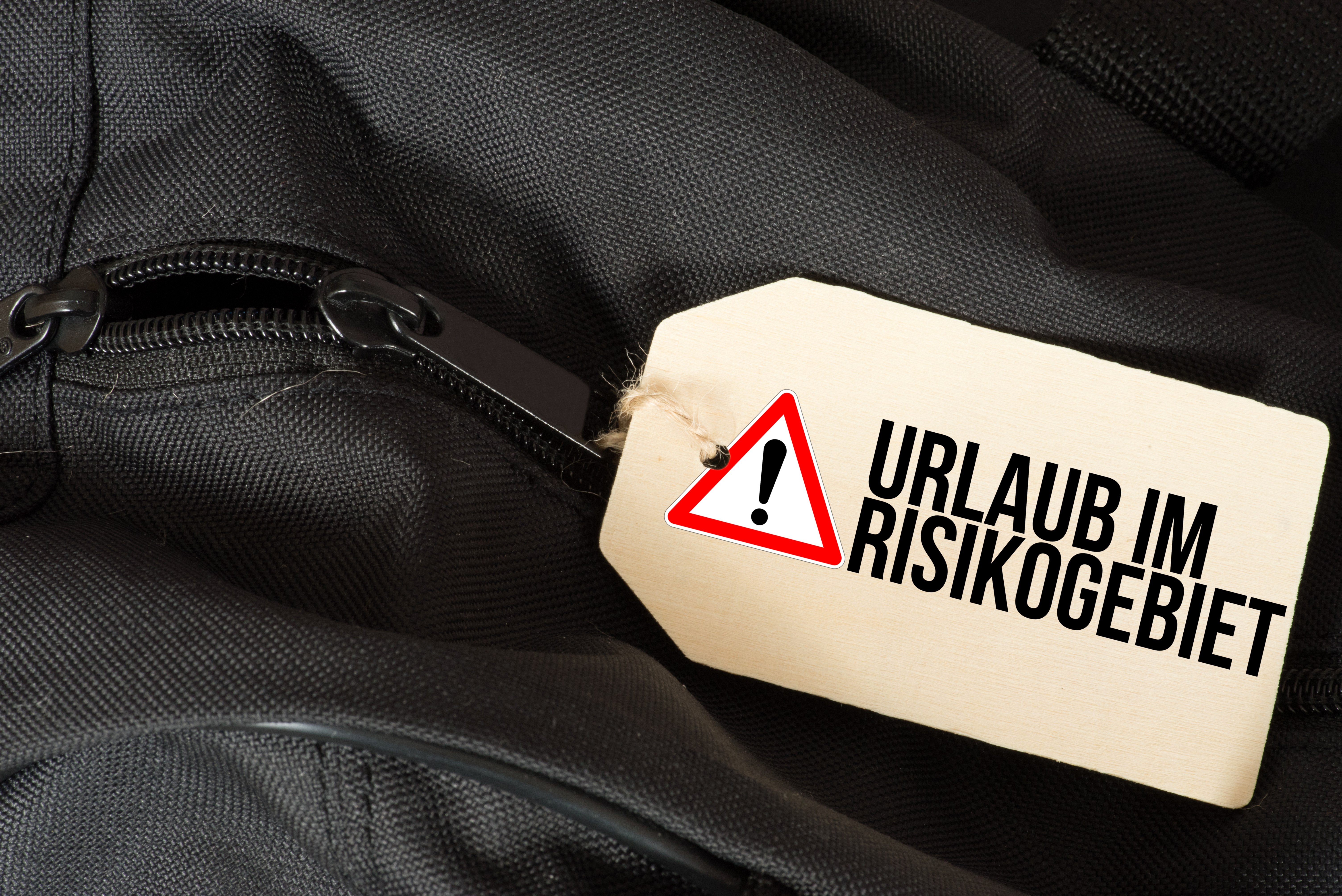 Reisetasche mit Schild mit der Aufschrift "Urlaub im Risikogebiet"