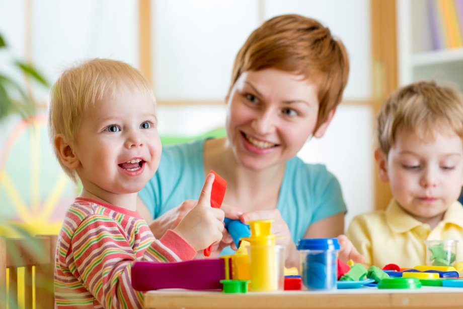 Kleinkinder und ihre Erzieherin spielen mit Knete 