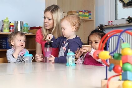 Erzieherin am Tisch Kinder trinken aus Trinkflasche mit Spielzeug
