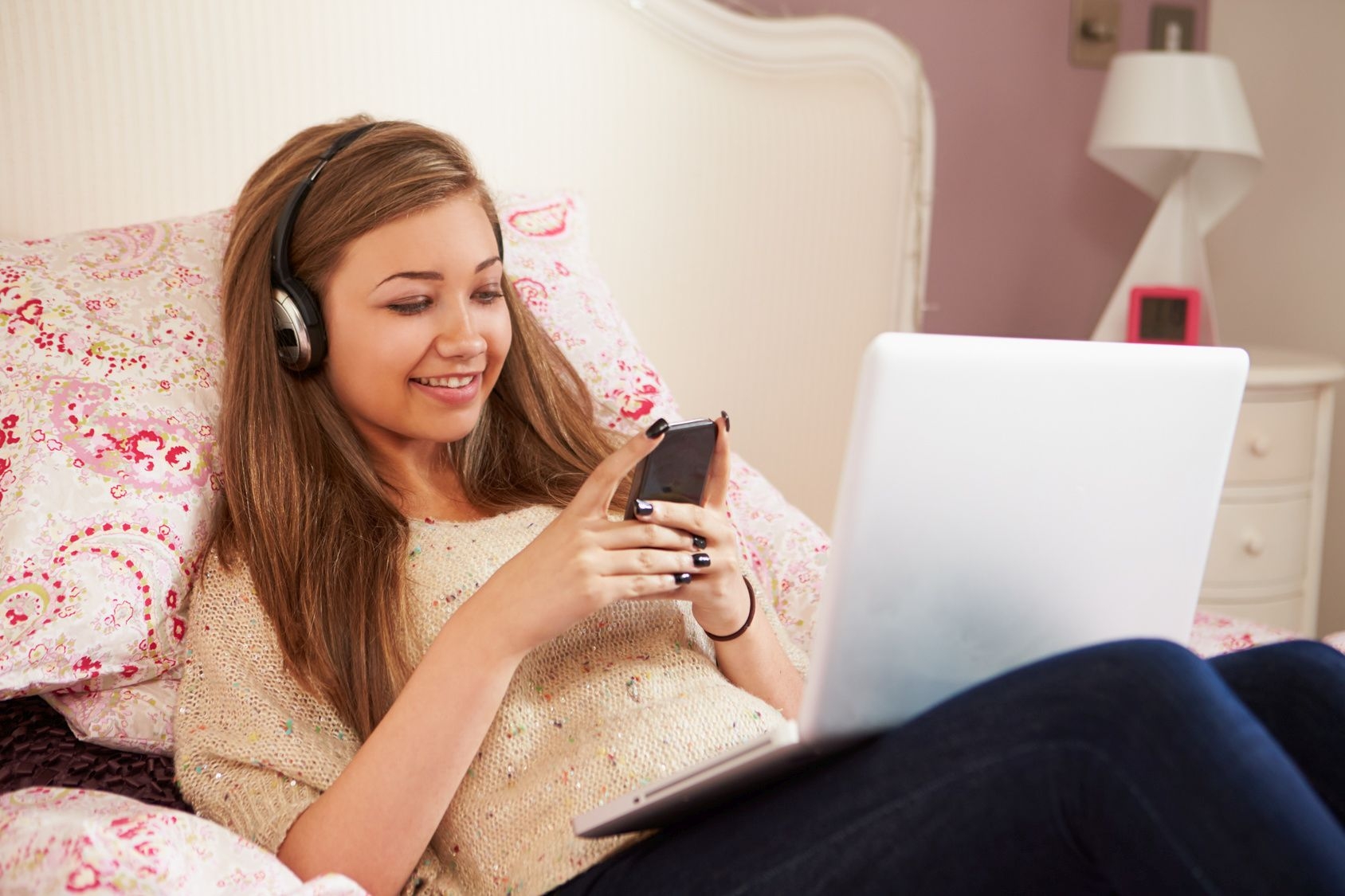 Teenage Girl Lying On Bed Using Laptop Whilst Texting