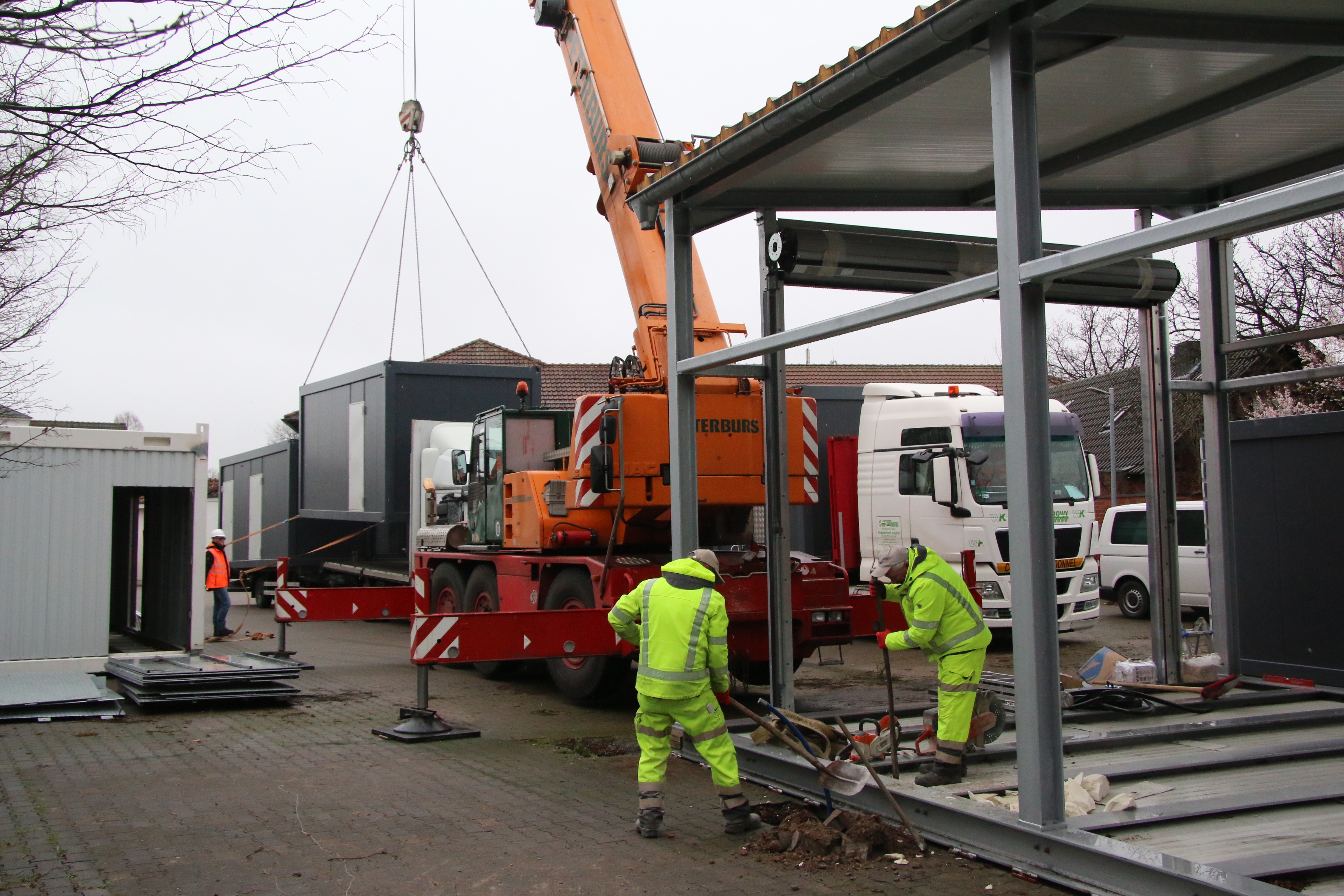 Per Kran wurden die sieben Container zunächst von Lkw gehoben und spä-ter an ihren Bestimmungsort gehievt. Im Vordergrund bearbeiten zwei Handwerker derweil die Anschlüsse an der künftigen Fahrzeughalle der Rettungswache.