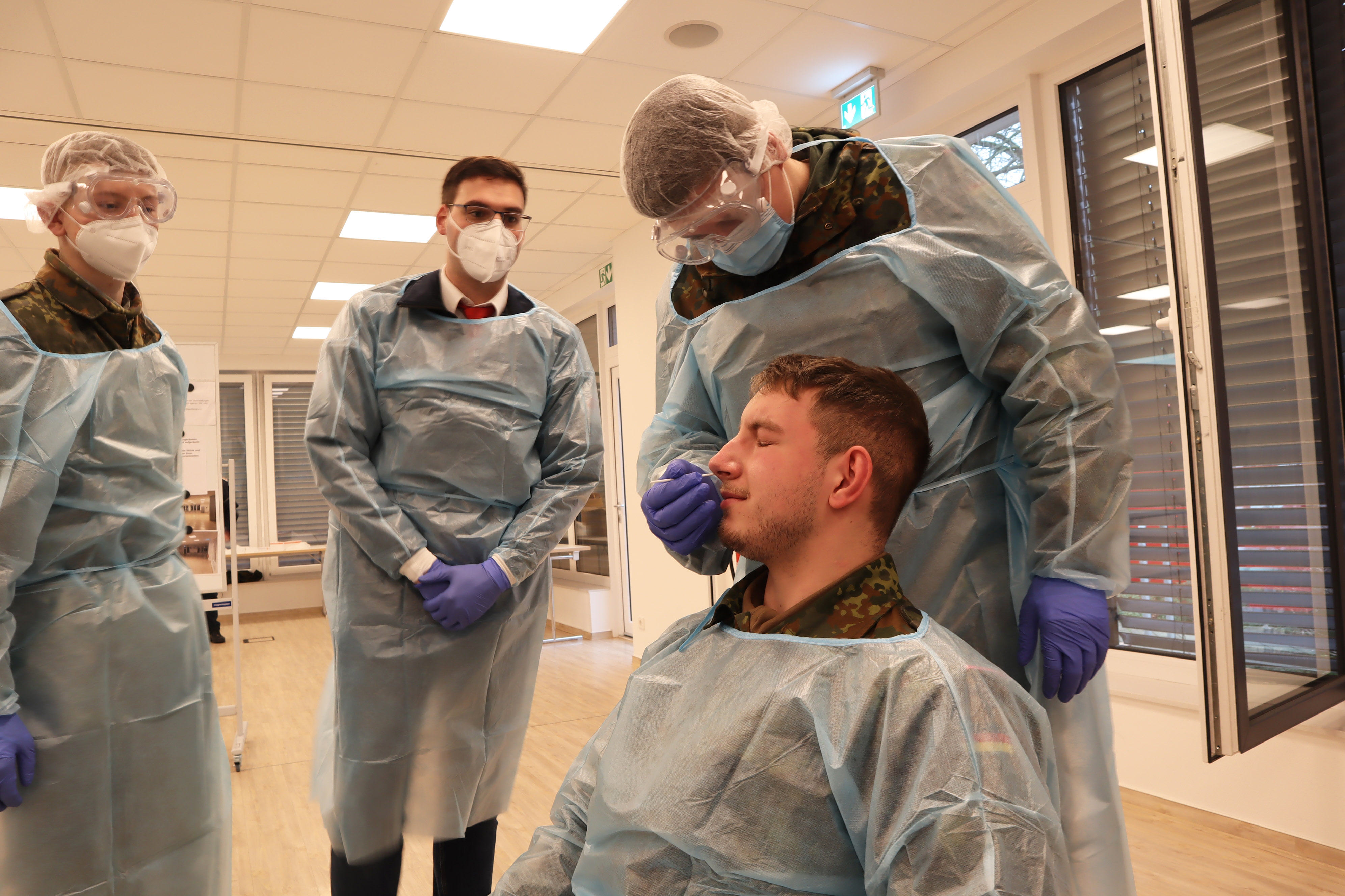 DRK-Schulung Soldaten Selbstversuch Ein Bundeswehrsoldat führt das Teststäbchen in die Nase seines Kameradens. Die Testperson sitzt auf einem Stuhl, die andere Person steht dahinter.