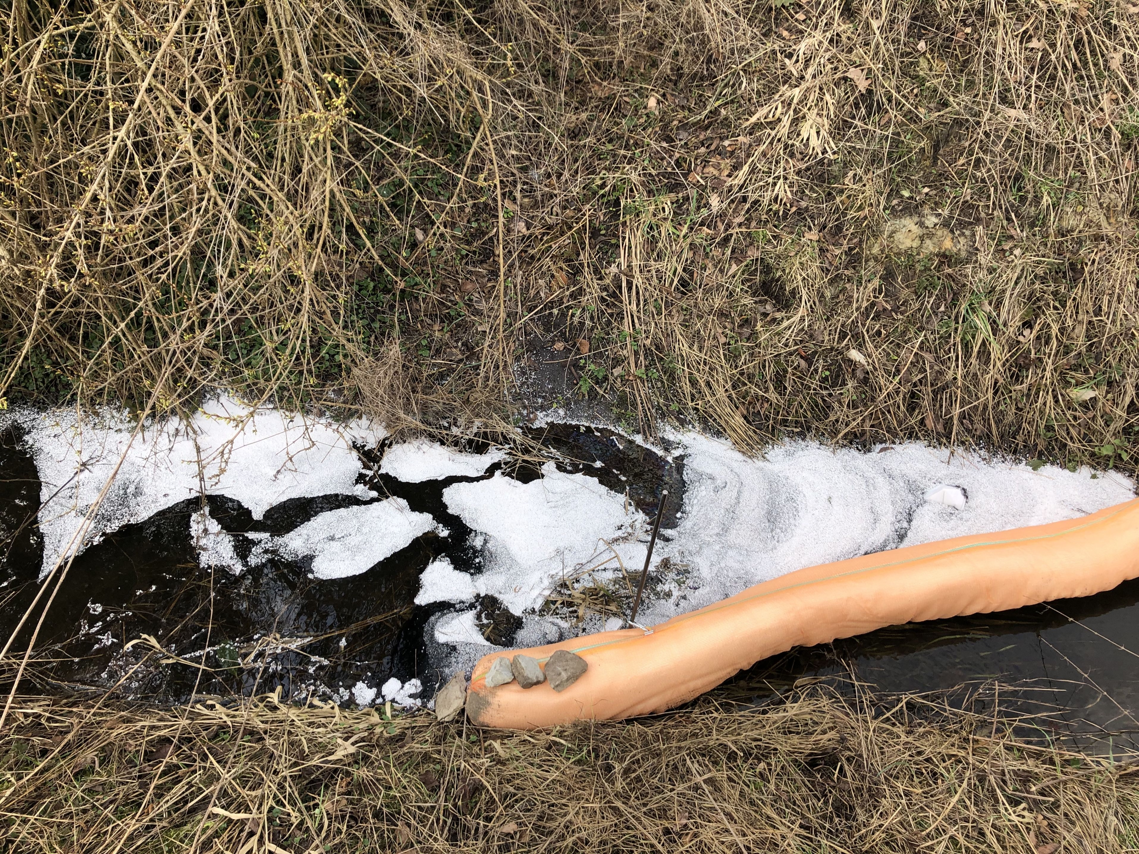 Die Feuerwehr errichtete Ölsperren im Aabach, sodass sich das Öl nicht weiter in Gewässern ausbreitet. Bei den weißen Kügelchen handelt es sich um spezielles Ölbindemittel für Gewässer. 