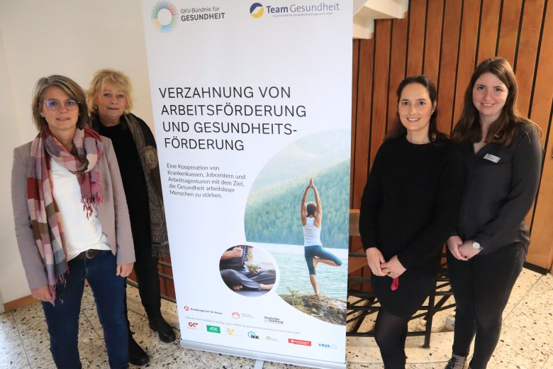 4 Personen stehen neben einem Roll-Up im Raum. 