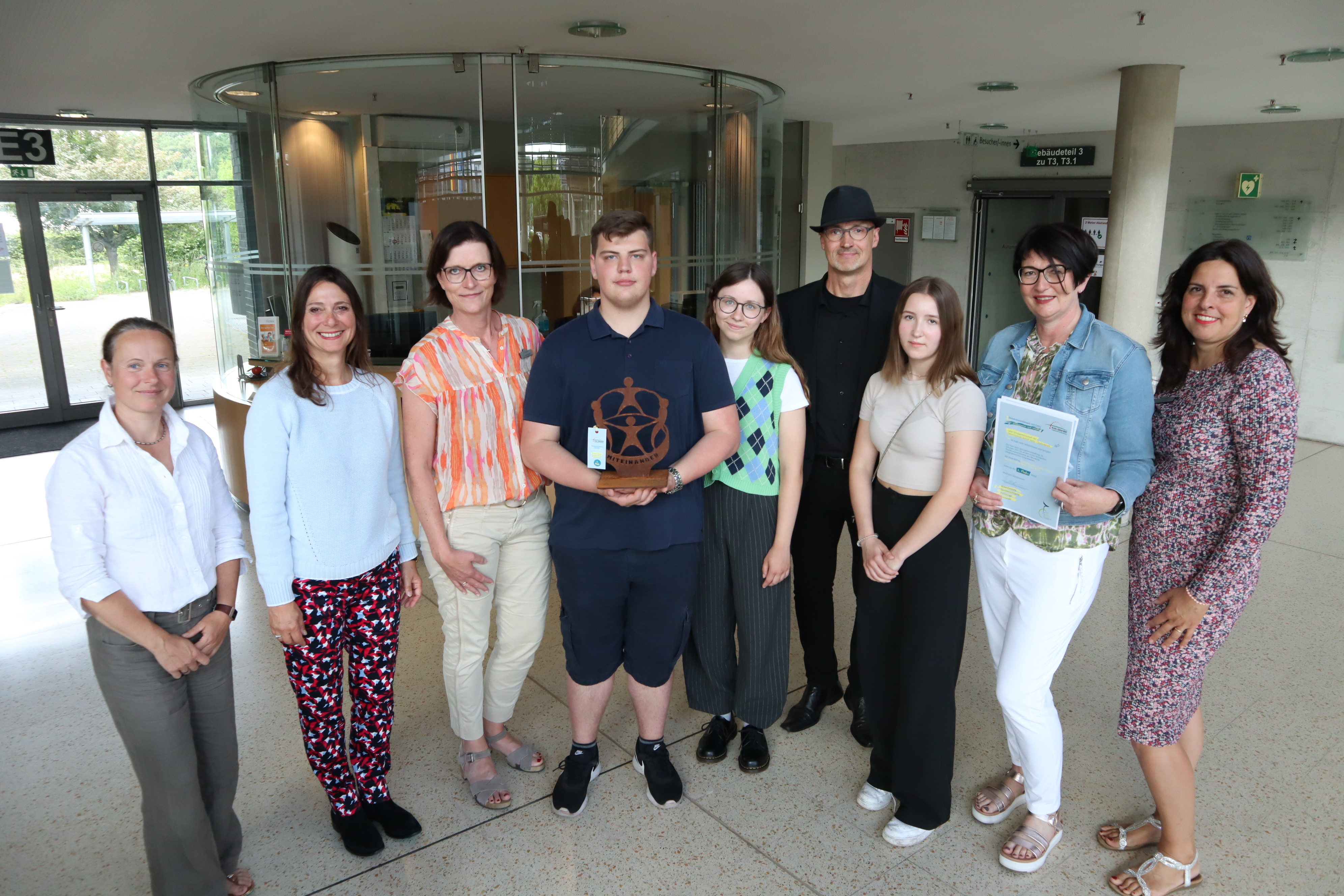 Feiern zusammen den Sieg der Gesamtschule Schloß Holte-Stukenbrock: (v.l.) Alexandra Molske und Ira Herdmann (Bildungs- und Schulberatung), Sandra Jürgenhake (Leiterin Abteilung Bildung), die Schüler Henry Solz und Larissa de Vlaming, Künstler Hans Kordes, Schülerin Carmen Aschof mit Schulleiterin Daniela Hartmann und Claudia Brhel (Bildungs- und Schulberatung). Die Siegergruppe des Demokratiewettbewerbs im Foyer des Kreishauses Gütersloh.