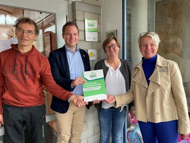 4 Personen stehen im Eingangsbereich des Kindergartens. Sie halten eine Plakette in den Händen.