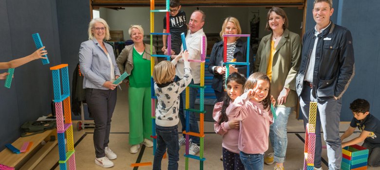 Mehrere Erwachsene stehen in einer Reihe, vor ihnen sind spielende Kinder zu sehen. 