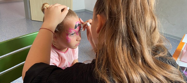 Einem Kind wird auf dem Sommerfest des Pflegekinderdienstes ein Flamingo ins geschminkt. 