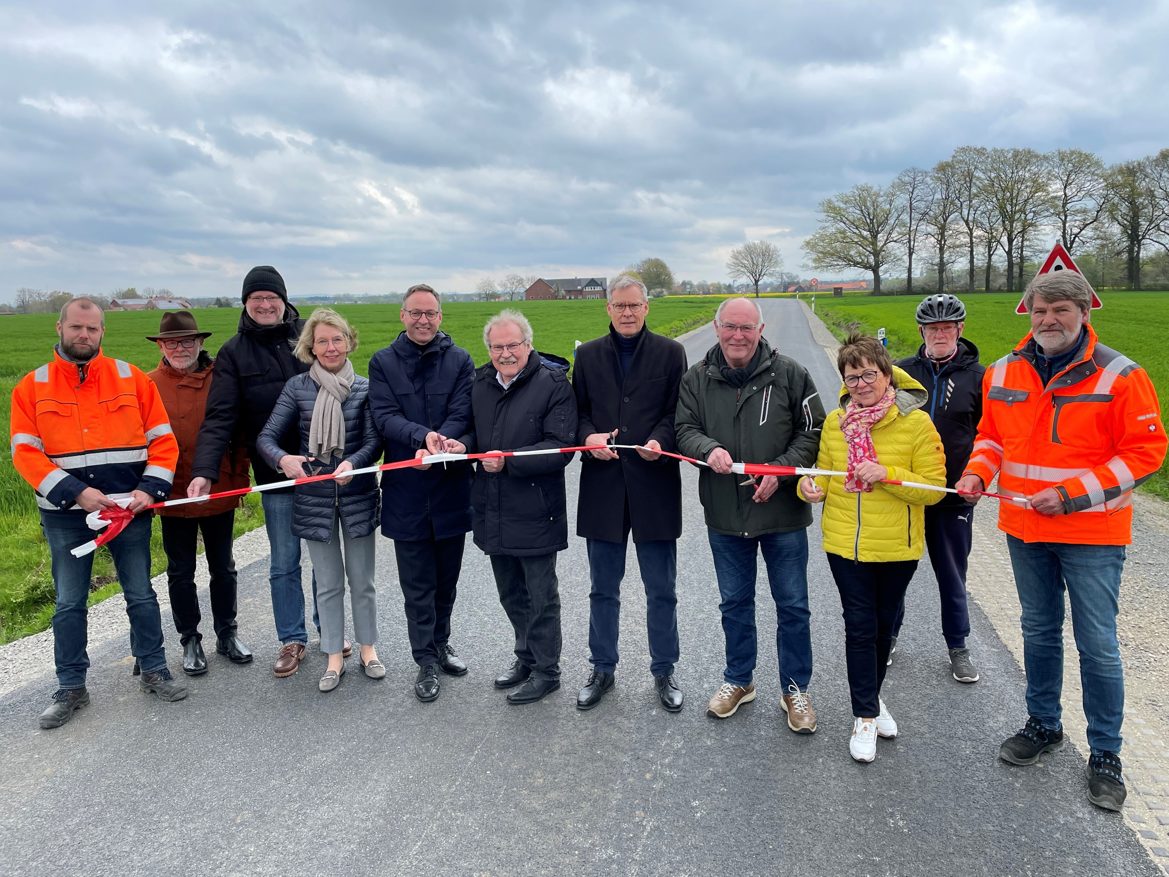 Geben den Wieksweg offiziell für den Verkehr frei: (v.l.) Bodo Brückner (zu-ständiger Bauleiter, Kreis Gütersloh), Alfred Kontermann (Kreistagsmitglied, SPD), Johannes Brinkrolf (Kreistagsmitglied, AfD), Henrika Küppers (Kreis-tagsmitglied, CDU), Bürgermeister Theo Mettenborg, Bernhard Altehülshorst (Kreistagsmitglied, CDU), Landrat Sven-Georg Adenauer, Heinz-Georg Großerohde (Kreistagsmitglied, CDU), Elisabeth Witte (Kreistagsmitglied, CDU), Heinz Lange (Mitglied beim ADFC) und Georg Stiens (zuständiger Bauleiter, Kreis Gütersloh). Personen, die ein Absperrband in der Hand halten und dies mit einer Schere durchtrennen.