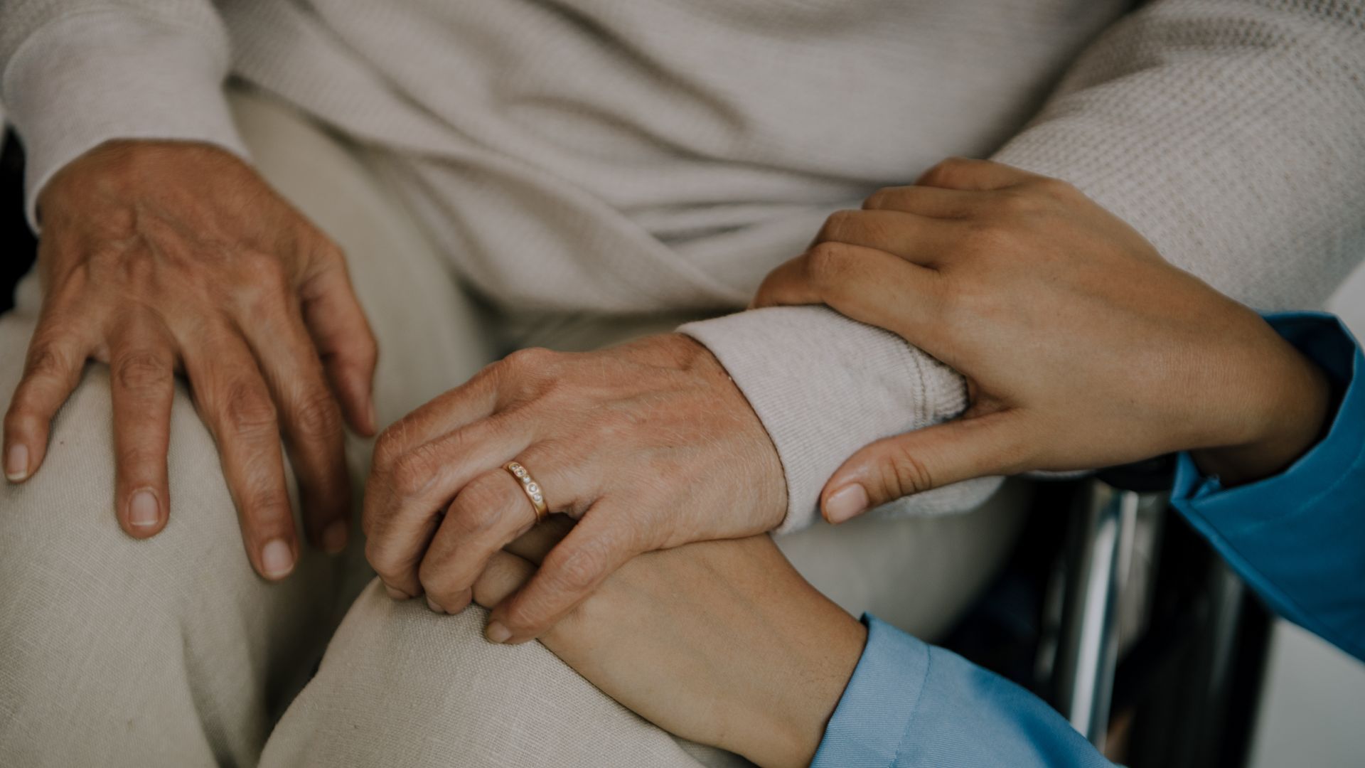 Hände eines alten Menschens, die von Händen eines jungen Menschens gehalten werden