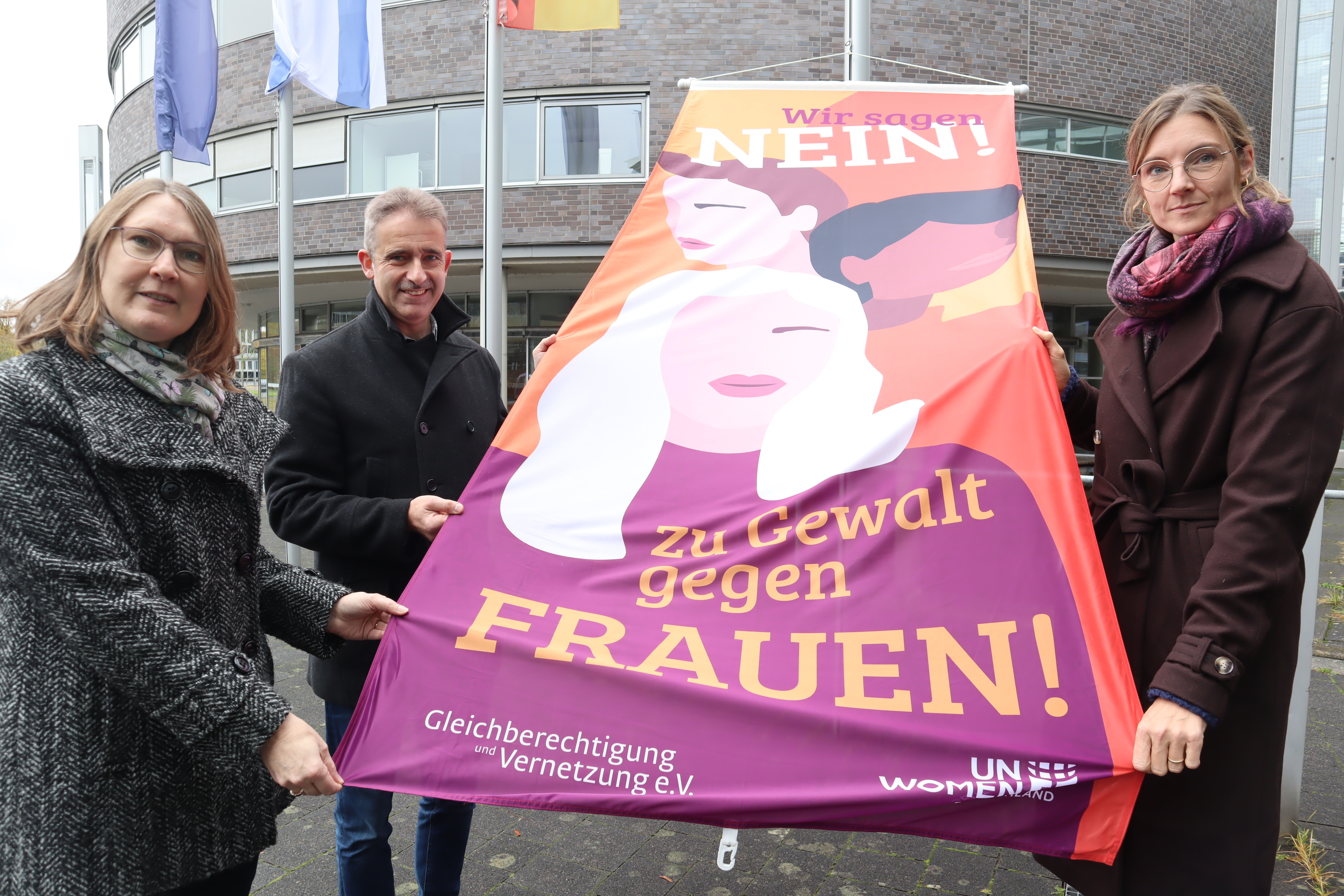 (v.l.) Kreisdirektorin Susanne Koch, Andreas Schröder (Opferschutz der Kreispolizeibehörde) und Gleichstellungsbeauftragte Angela Wüllner zeigen die Flagge, die ein Zeichen gegen Gewalt an Frauen setzen soll.