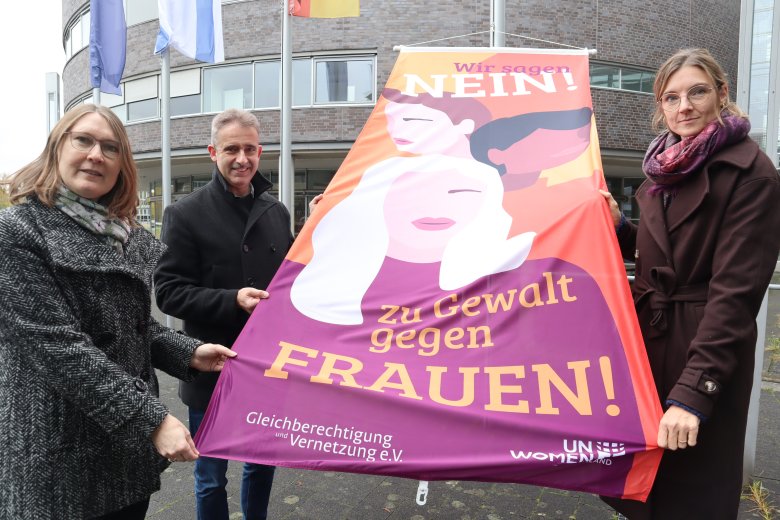 (v.l.) Kreisdirektorin Susanne Koch, Andreas Schröder (Opferschutz der Kreispolizeibehörde) und Gleichstellungsbeauftragte Angela Wüllner zeigen die Flagge, die ein Zeichen gegen Gewalt an Frauen setzen soll. 