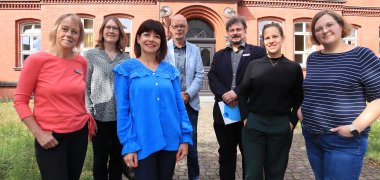 Sieben Erwachsene, die vor der Volkshochschule Gütersloh stehen. 