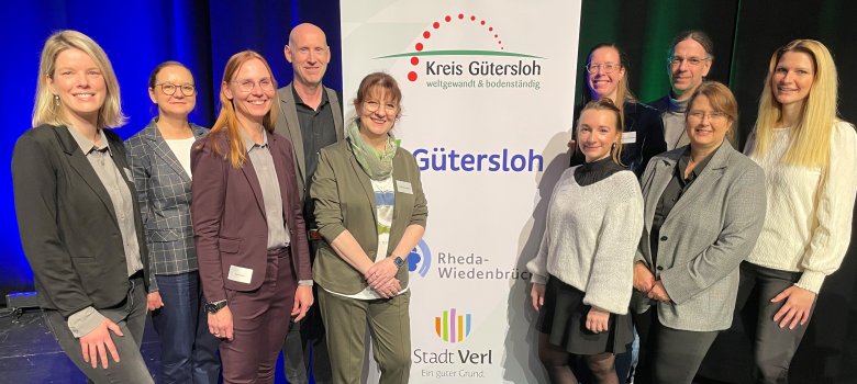 Die Organisatoren der Kinderschutzkonferenz stehen in der Stadthalle Gütersloh vor einem Banner