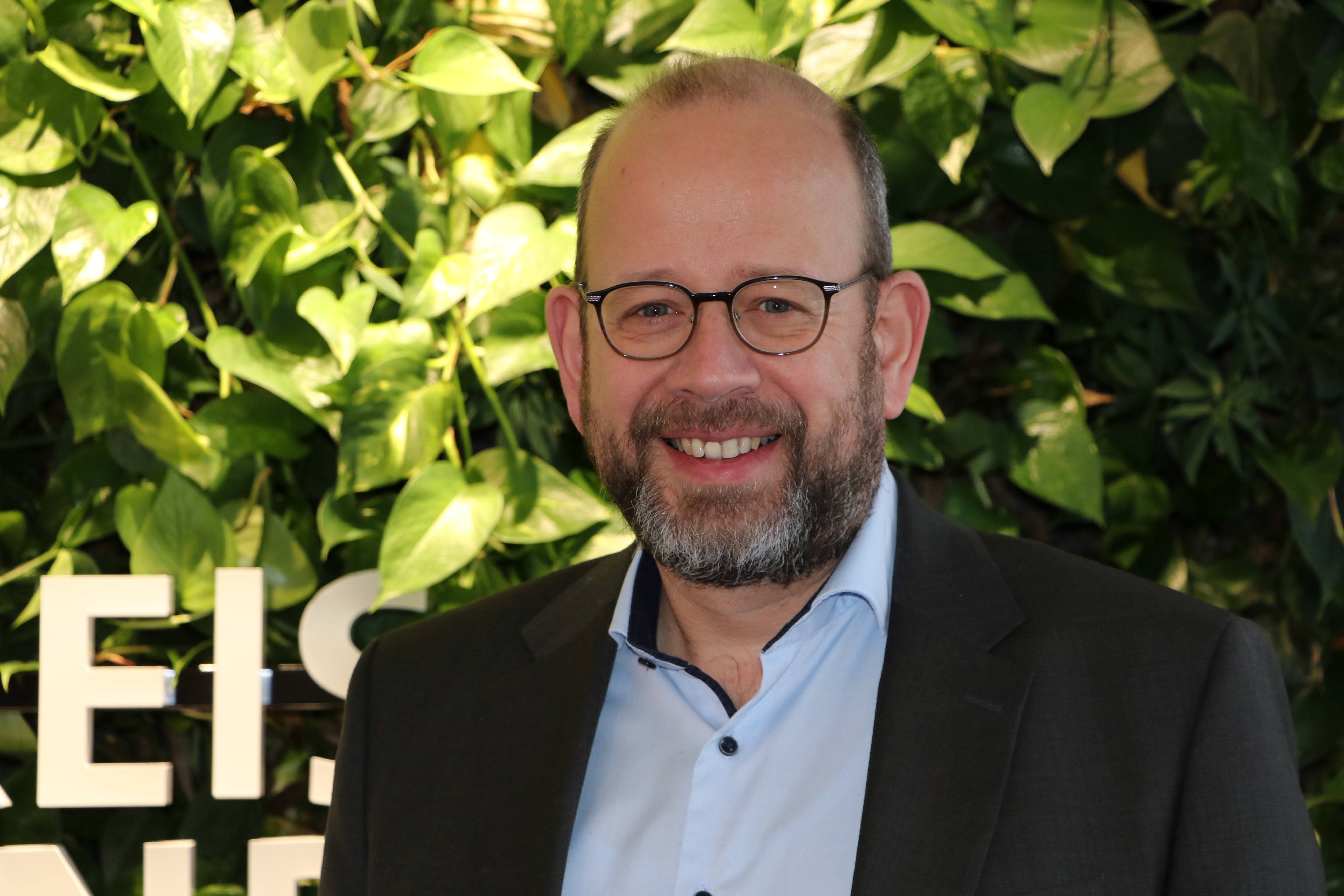 Dr. Herbert Bleicher Dr. Herbert Bleicher - Portraitfoto vor Grünpflanzen und Buchstabenfragmenten des Schriftzugs 'Kreis Warendorf'.
