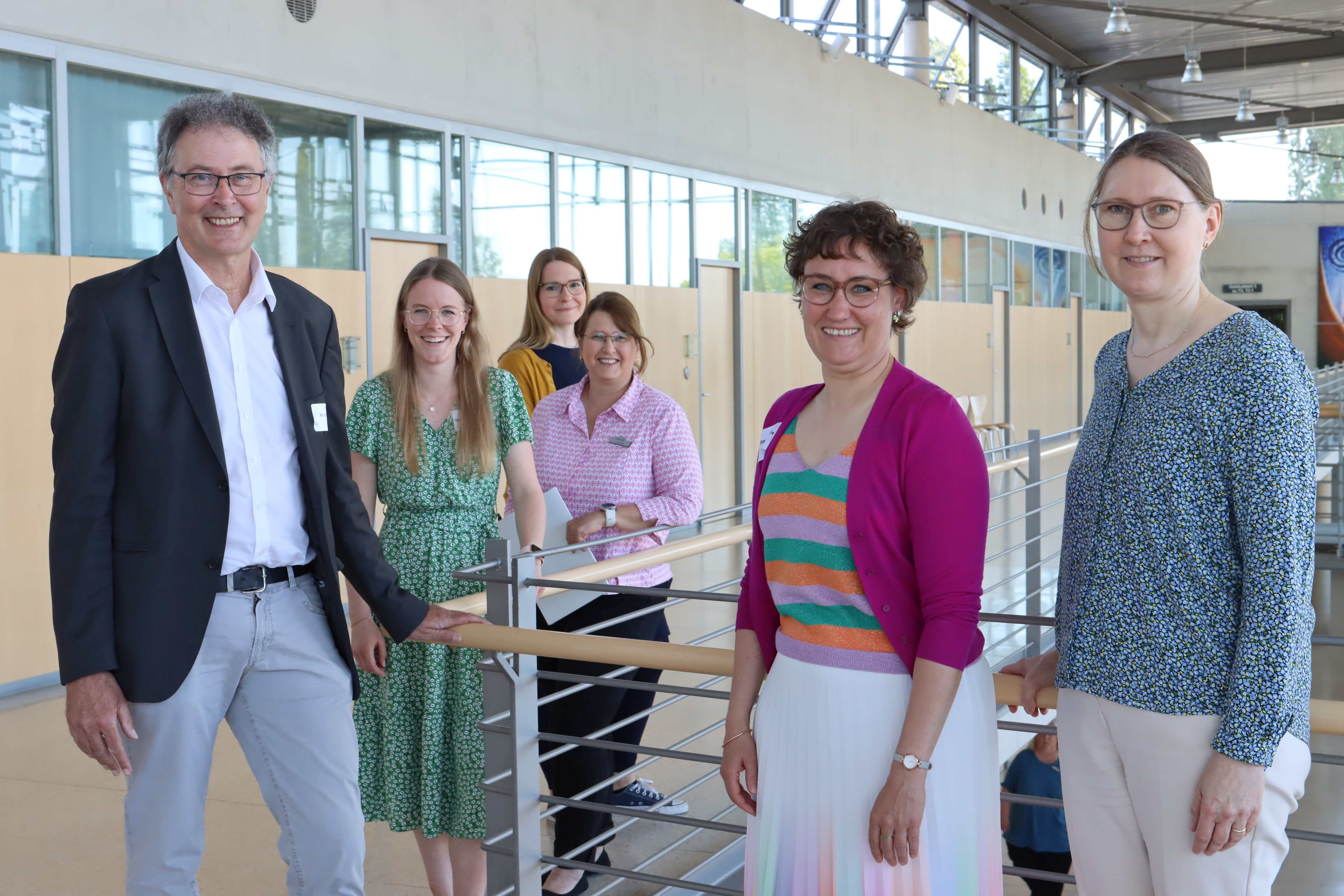 Sechs Personen stehen nebeneinander, teilweise versetzt, und blicken in die Kamera.