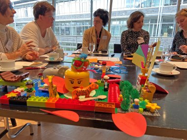 Im Vordergrund ist ein Lego-Modell zu sehen. Im Hintergrund tauschen sich fünf Frauen aus.