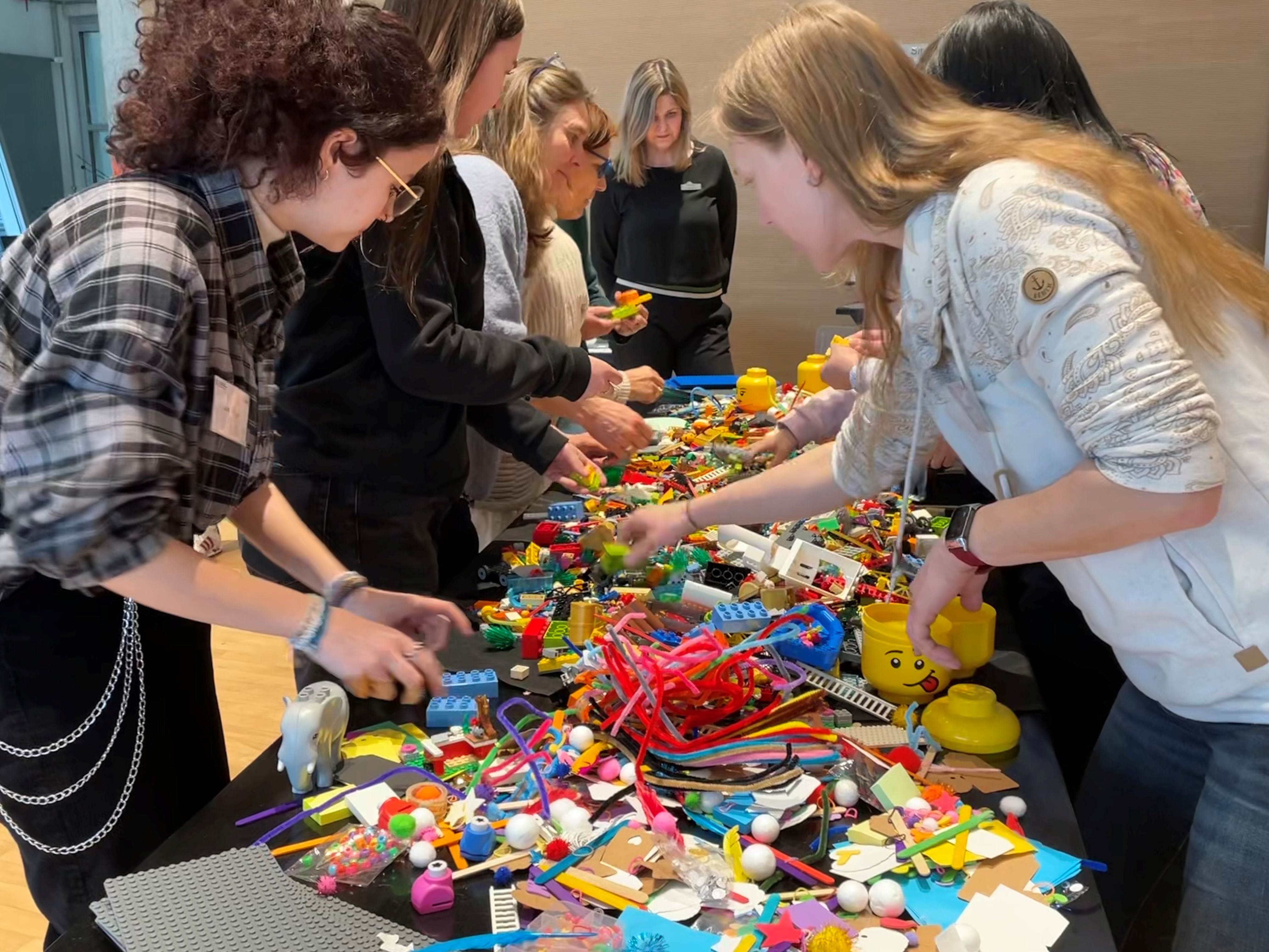 Menschen stehen an einem Tisch, der mit vielen einzelnen Lego-Bausteinen bedeckt ist.