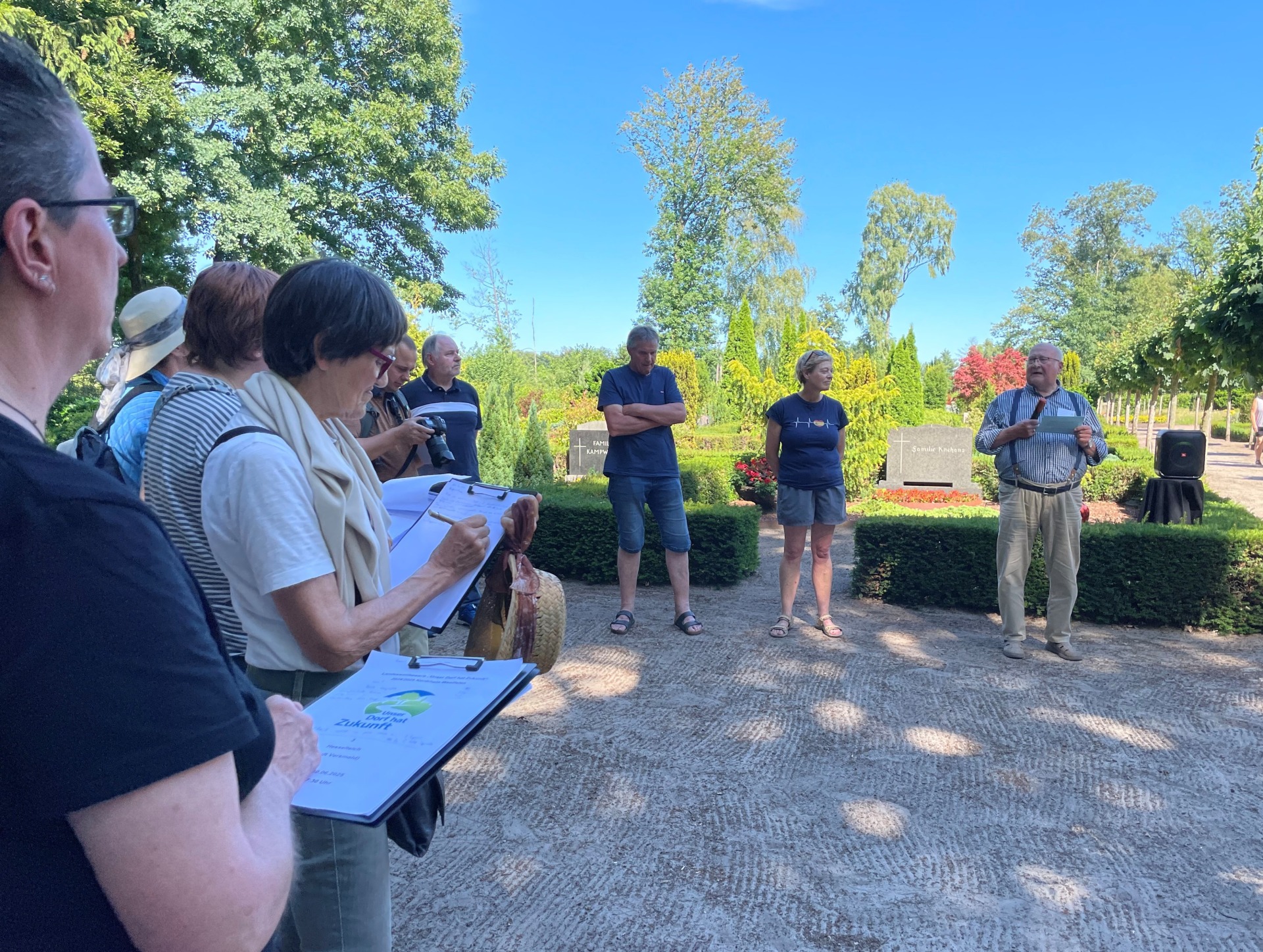 Gruppe am Friedhof in Hesselteich. Personen halten Klemmbretern in den Händen und notieren sich etwas.