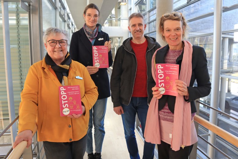 Vier Personen stehen nebeneinander und halten eine Broschüre in den Händen. 