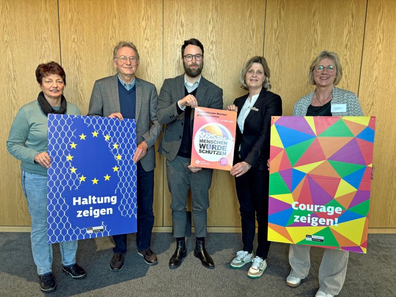 Fünf Personen präsentieren ein Plakat zu den Internationalen Wochen gegen Rassismus 2025