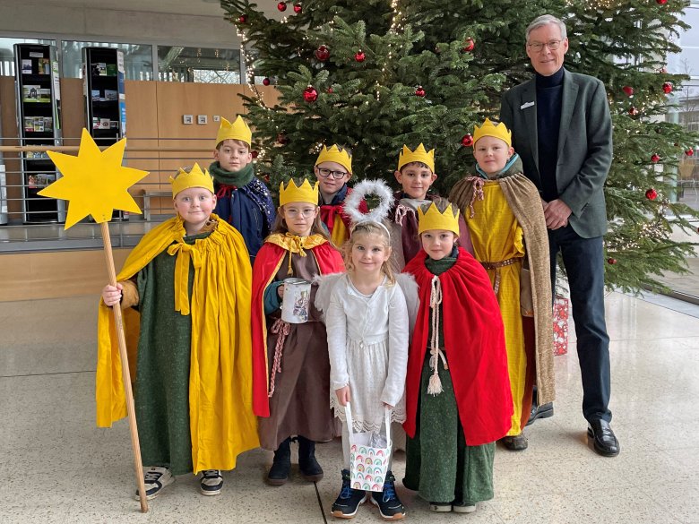 Acht Kinder stehen verkleidet neben Landrat Adenauer vor dem Weihnachtsbaum.