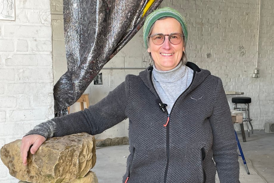 Neben Steinen steht die Künstlerin in ihrem Atelier. 