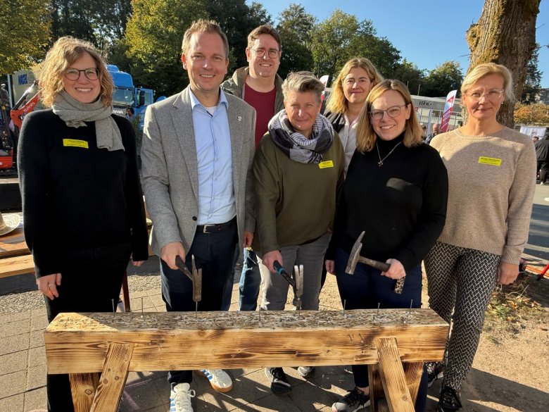 Eine Personengruppe schlägt mit Hammer Nägel in ein Holzbrett