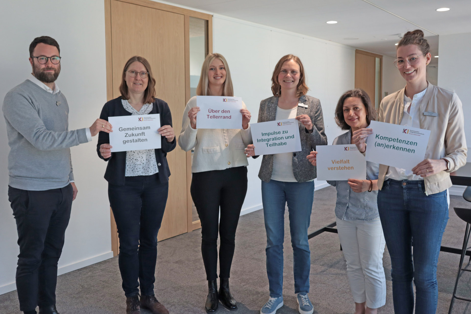 Personen stehen nebeneinander und blicken in die Kamera, halten Zettel in den Händen.