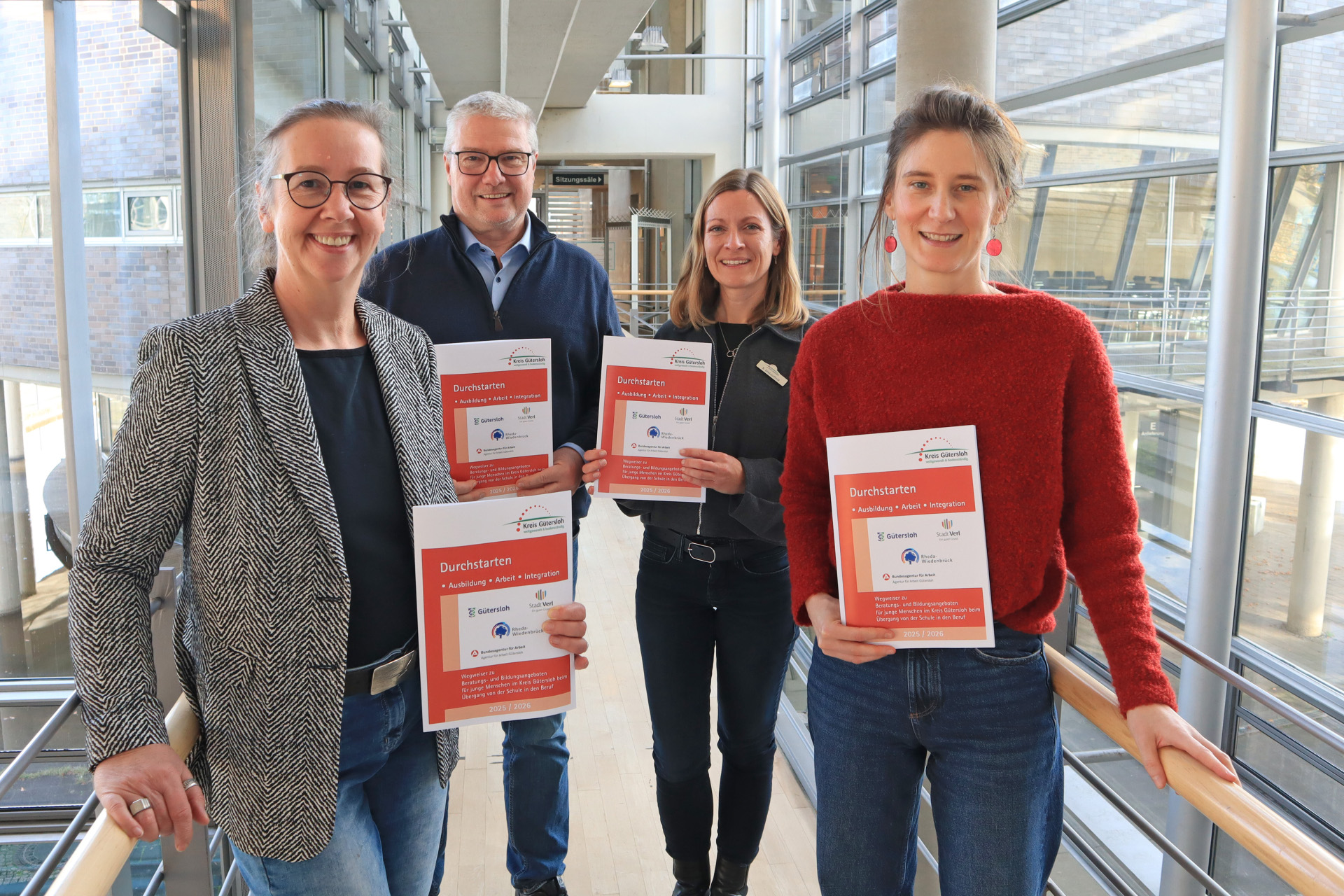 Personen stehen nebeneinander, blicken in die Kamera und halten den aktualisierten Wegweiser in den Händen.