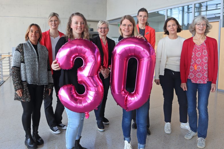Acht Frauen stehen nebeneinander, zwei von Ihnen halten eine 30 als Folienluftballons in den Händen. 