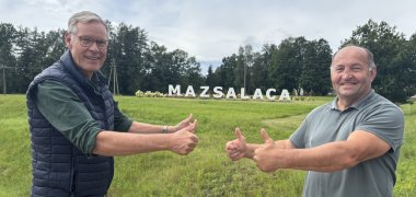 Zwei Männer vor einem Schriftzug mit Daumen nach oben