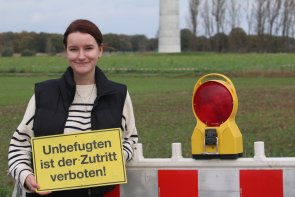 Person steht vor einer Absperrung und hält ein Schild mit der Aufschrift 'Unbefugten ist der Zutritt verboten' in den Händen.