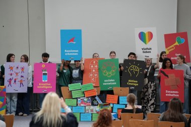 Jugendliche stehen auf einer Bühne nebeneinander und halten Plakate mit Aufschrift in den Händen.
