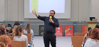 Referent beim Sprechen zwischen Stuhlreihen.