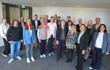 Personen stehen in einer Gruppe zusammen und blicken in die Kamera.