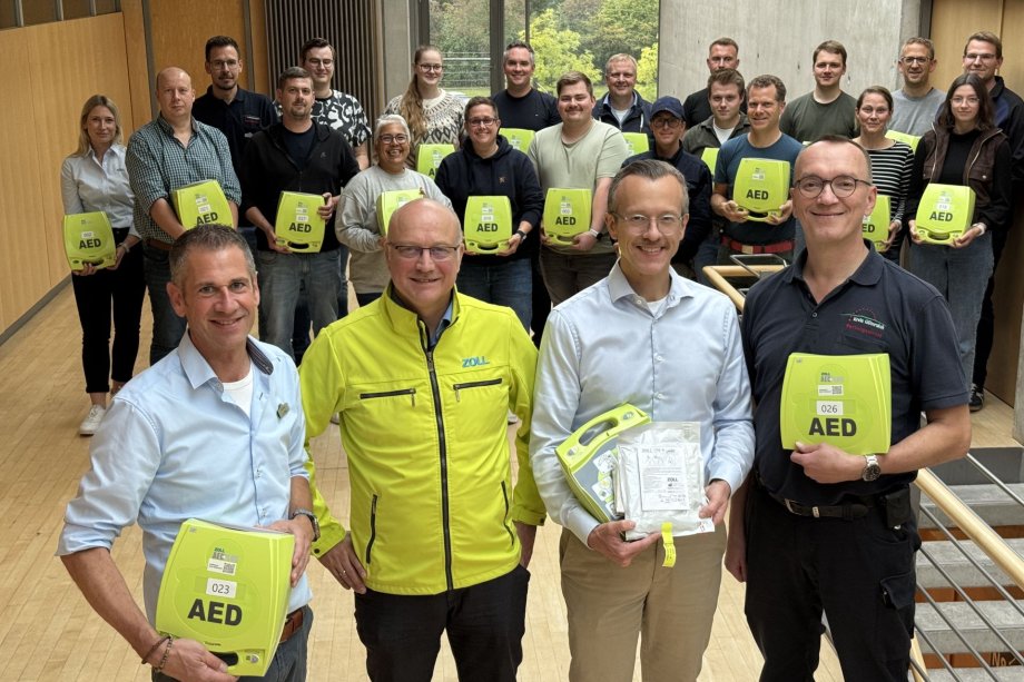 Defis für die Mobilen Retter Die ersten Mobilen Retter - hier im Hintergrund des Fotos zu sehen - haben ihre ‚Automatisierten Externen Defibrillatoren (AED)‘ erhalten, im Vordergrund (v.l.): Jürgen Theis (Leiter der Abteilung Bevölkerungsschutz), Andreas Cleve (Stiftung ‚Zoll Foundation‘), Dr. Gerrit Jansen (Leiter der Studie) und Dr. Bernd Strickmann (Ärztlicher Leiter Rettungsdienst Kreis Gütersloh).