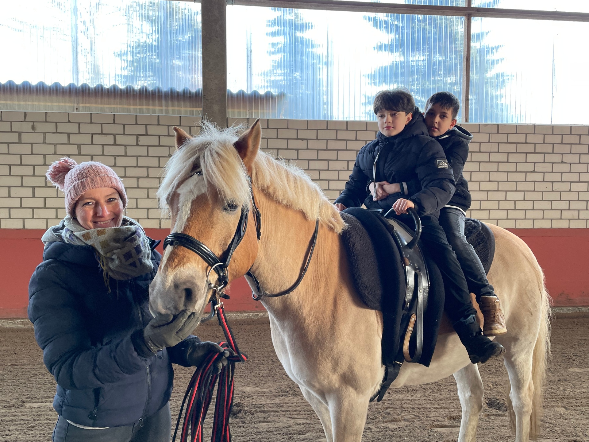 Zwei Schüler sitzen auf dem Pferd. Daneben eine erwachsene Person.