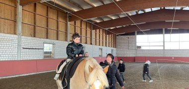 Schülerin sitzt auf einem Pferd Aaron und wird begleitet. 