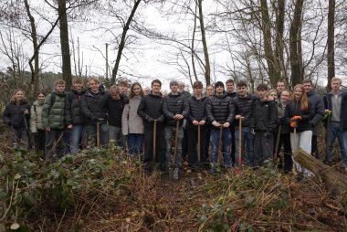 Gruppe mit Spaten in den Händen in einem Waldstück. 