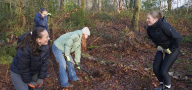 Schülerinnen graben in der Erde mit einem Spaten.