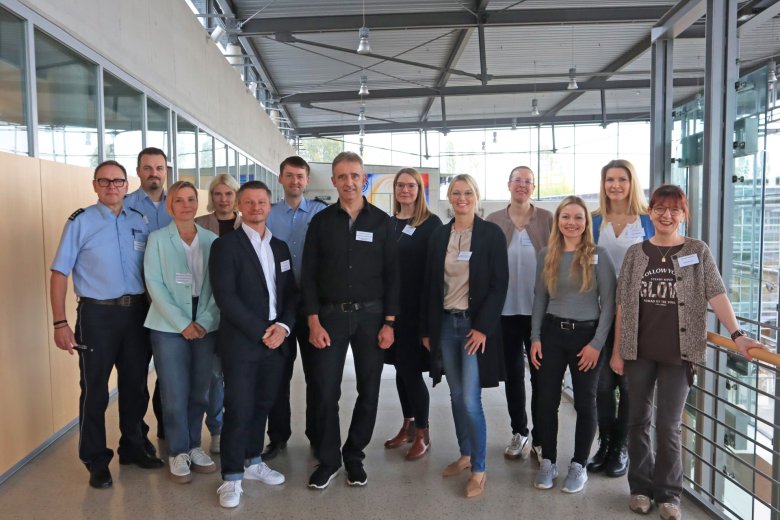 Personen stehen in einer Gruppe nebeneinander, teilweise in zwei Reihen hintereinander. Alle blicken in die Kamera.
