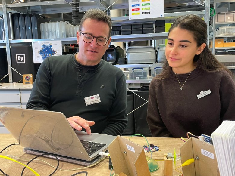 Eine Person erklärt einer anderen Person vor einem Laptop etwas.