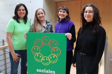 Vier Frauen blicken in die Kamera. In den Händen halten sie ein Plakat mit Smileys und der Aufschrift 'Soziales'.