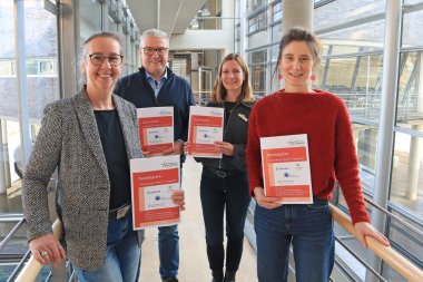 Personen stehen nebeneinander, blicken in die Kamera und halten den aktualisierten Wegweiser in den Händen.