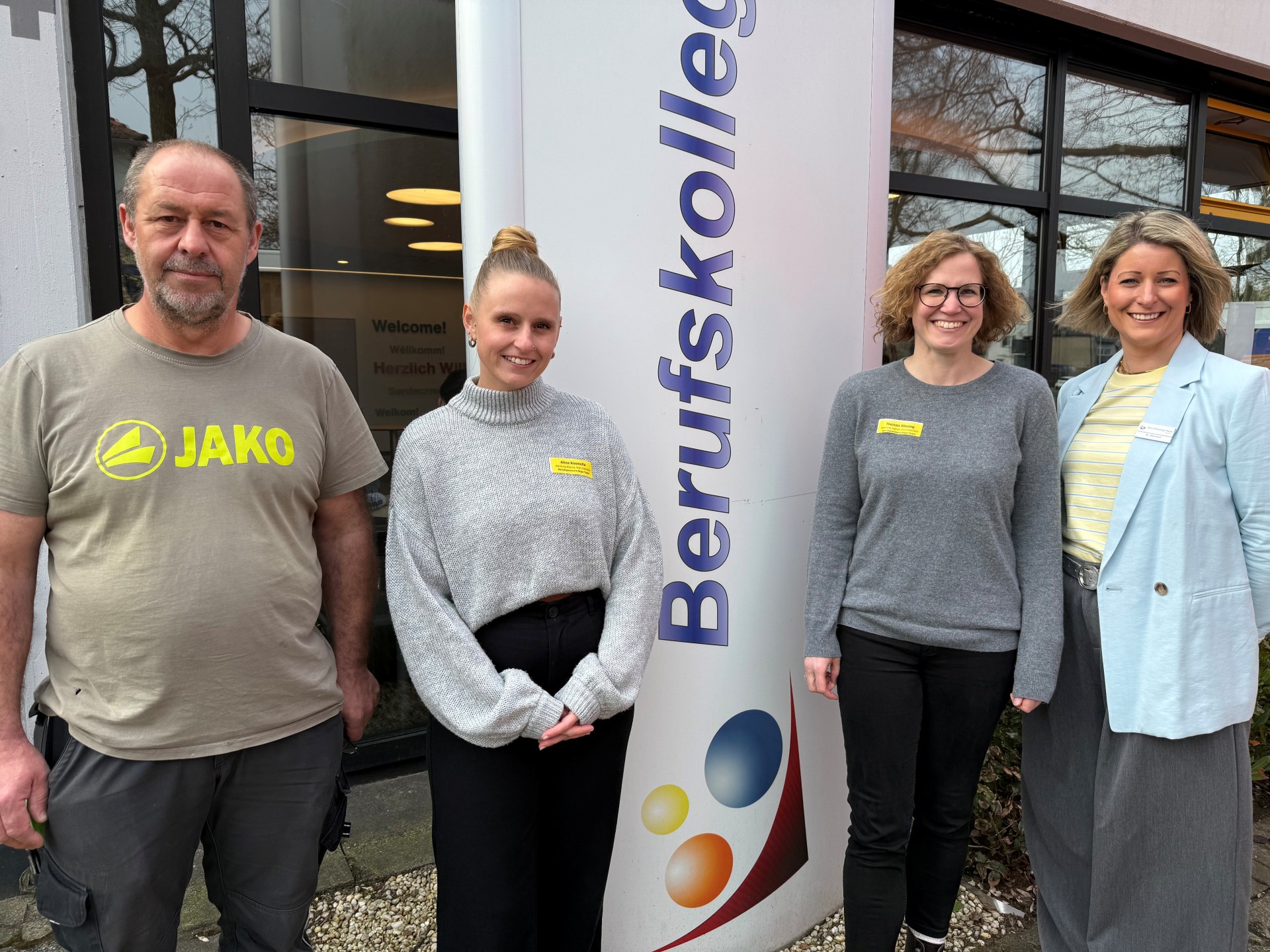 Vier Personen stehen vor dem Berufskolleg und schauen in die Kamera.