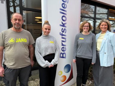 Vier Personen stehen vor dem Berufskolleg und schauen in die Kamera.