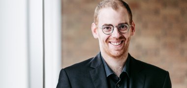 Ein Mann steht im Mittelpunkt und blickt in die Kamera. 