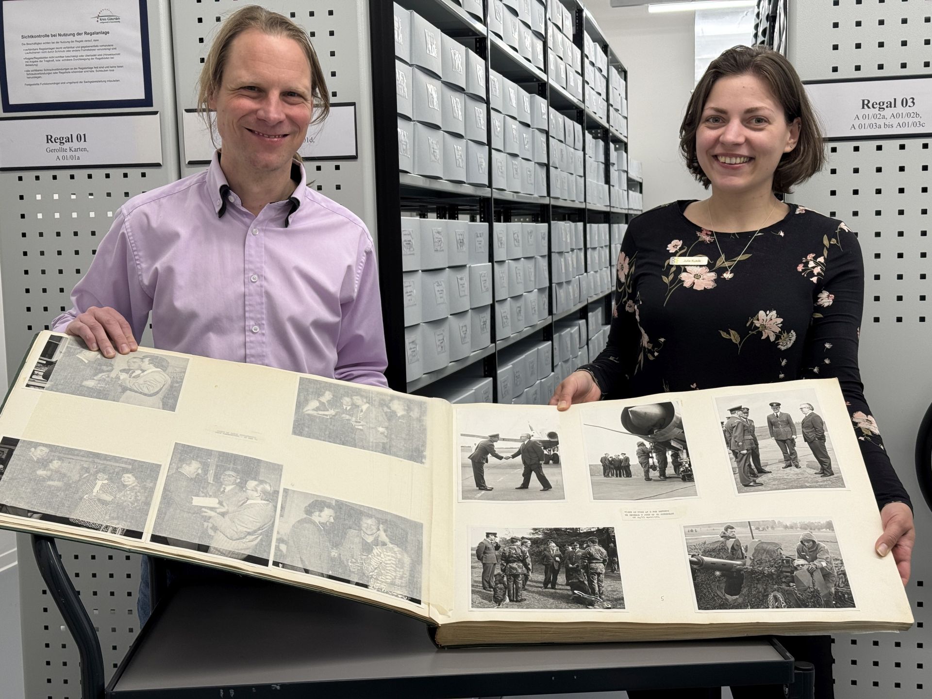 Julia Kuklik, Leiterin des Stadtarchivs, und Dr. Franz Jungbluth, Mitarbeiter des Kreisarchivs, präsentieren im magazinraum des Kreisarchivs ein Fotoalbum mit Schwarzweißaufnahmen der ehemals in Gütersloh stationierten britischen Streitkräfte. 