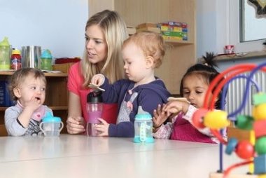 Erzieherin am Tisch Kinder trinken aus Trinkflasche mit Spielzeug